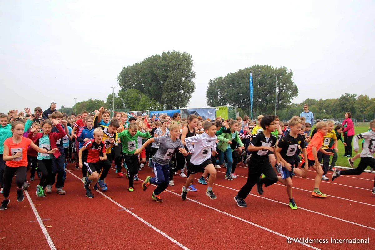 Large group of children running together on a red athletic track during an outdoor sports event.