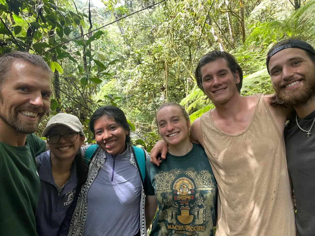 Grupo de seis personas sonriendo juntas en la exuberante selva verde de fondo.