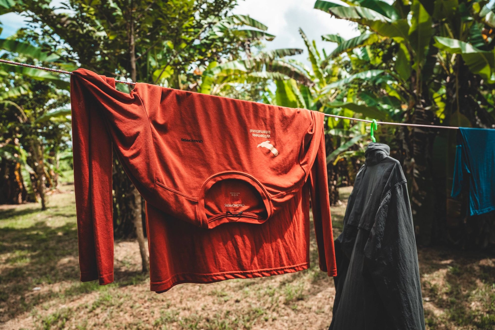 Woman in black clothing hangs red laundry on a clothesline surrounded by lush green foliage.