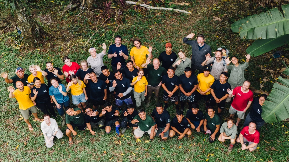Overhead view of a large group of approximately 50 people posing on green grass with raised hands.