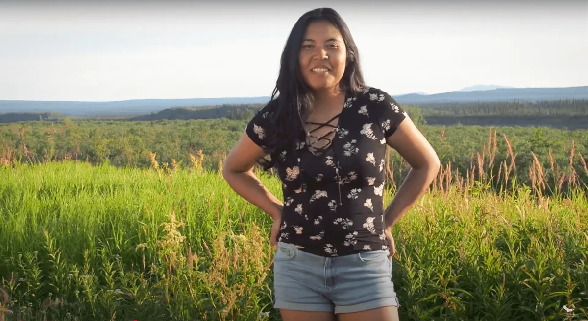 Young woman smiling at camera standing in a cornfield with forested landscape in the background.