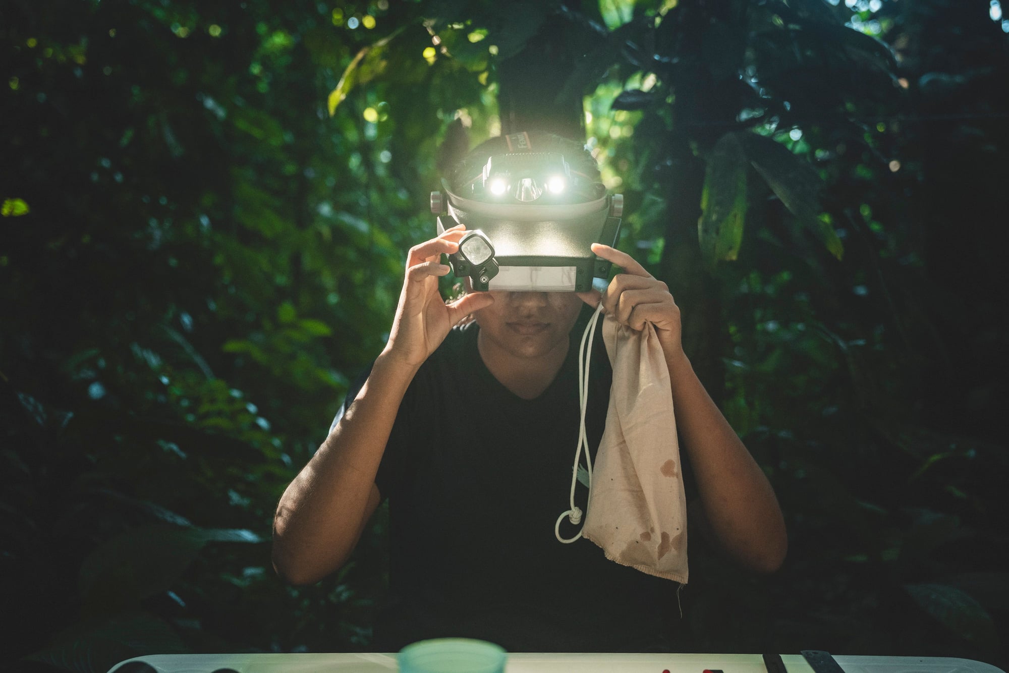 Person mit leuchtender Stirnlampe hält Kamera in dunklem Wald mit grünem Licht