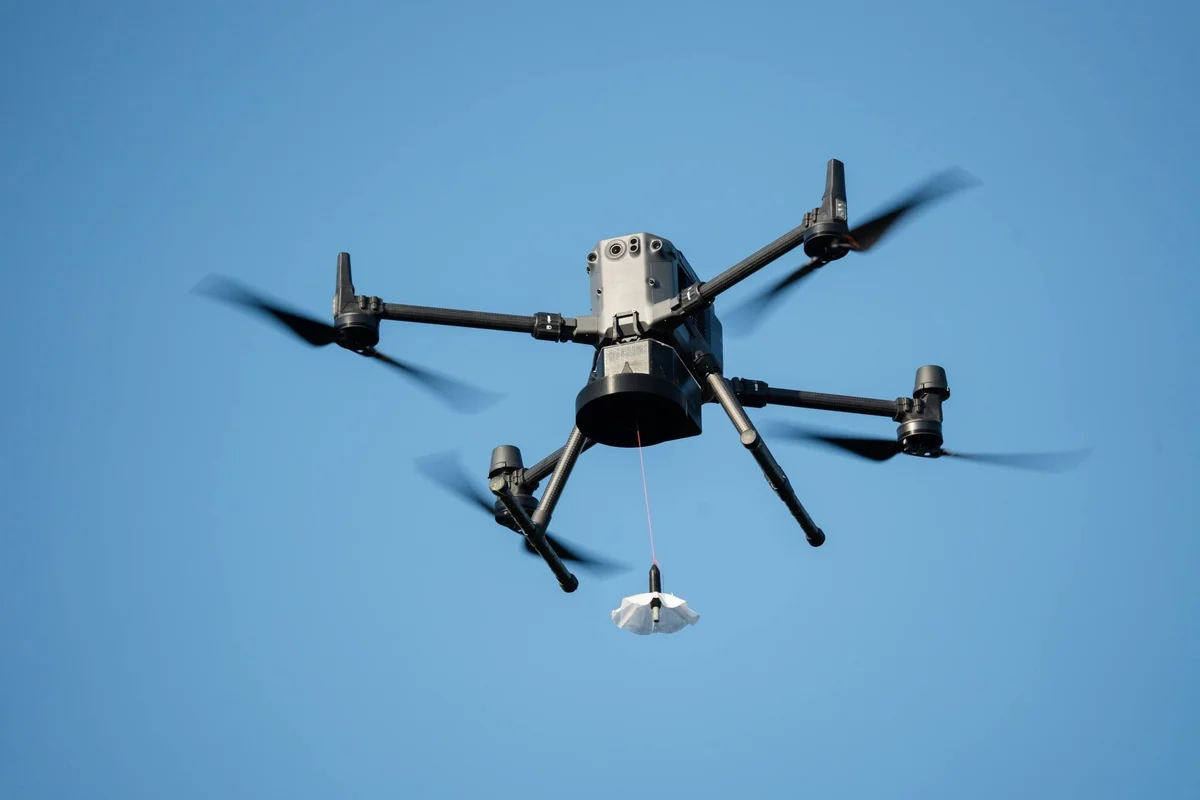 Quadcopter drone with four spinning rotors flying against clear blue sky