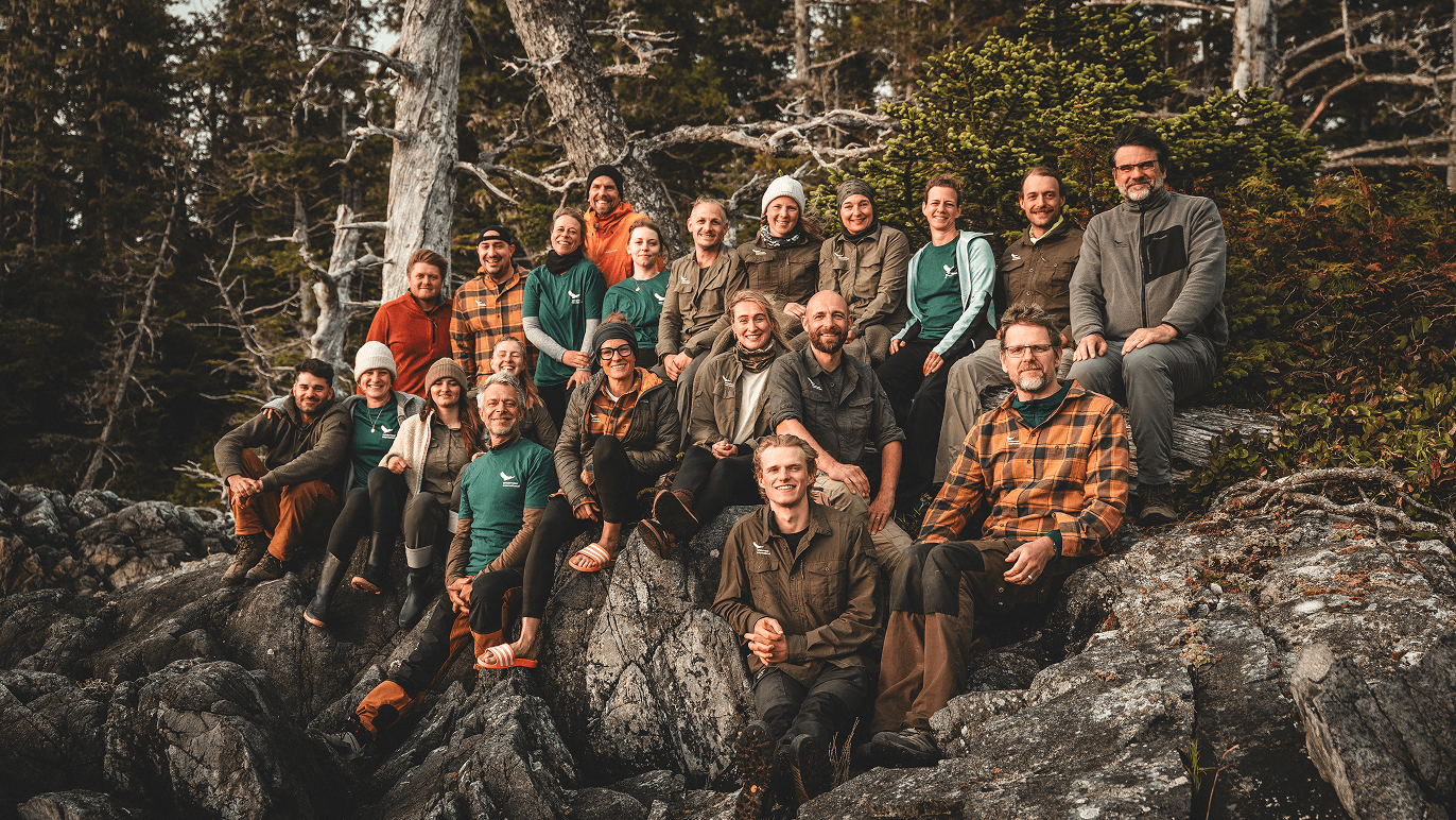 Large group of people posing together on rocks in a forest during autumn daylight.