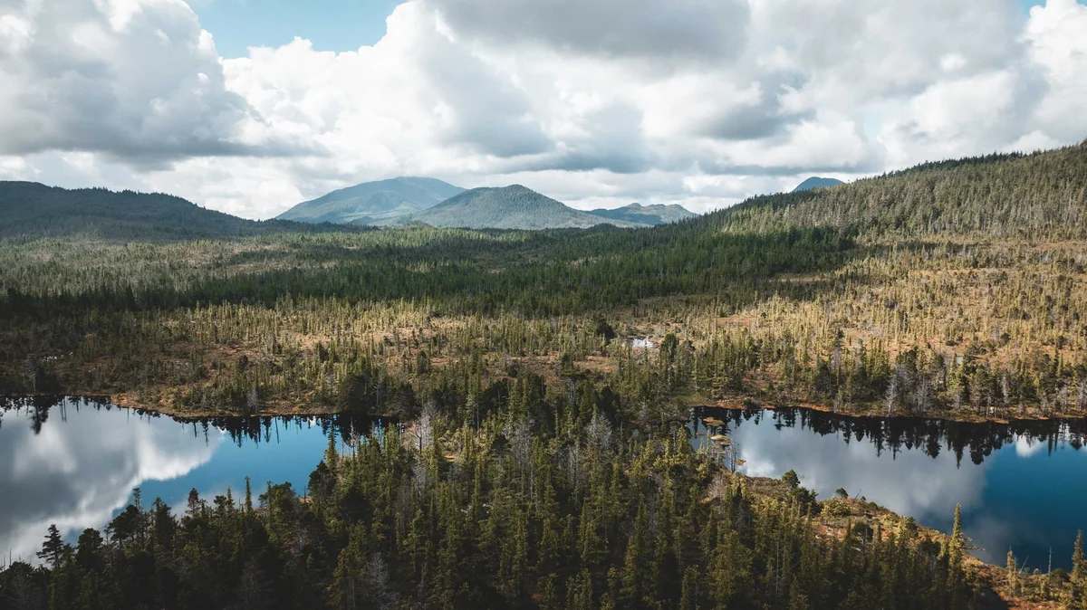Aerial view of a forested valley with two lakes, evergreen forests, and distant mountains under a partly cloudy sky.
