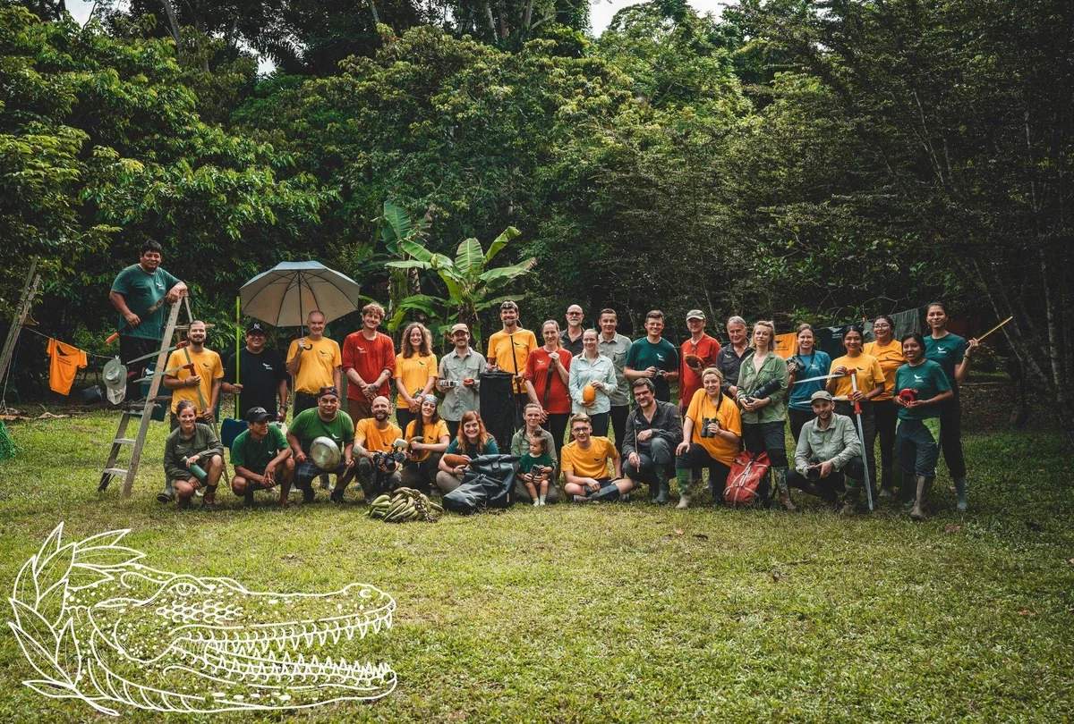 Large group of volunteers in yellow and coloured shirts posing for a group photo in a lush forest setting.