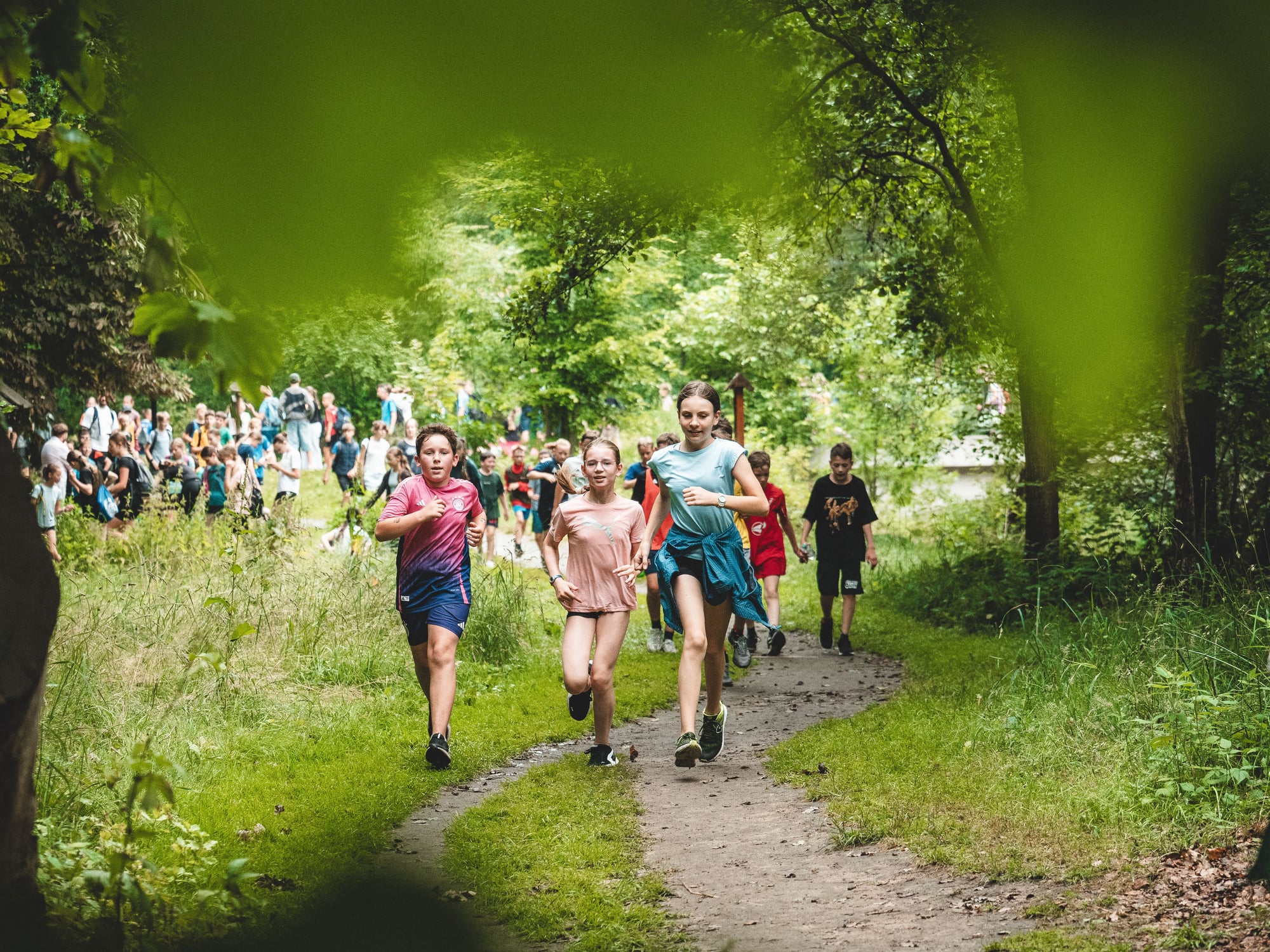Children running on a forest trail surrounded by lush green vegetation and trees.