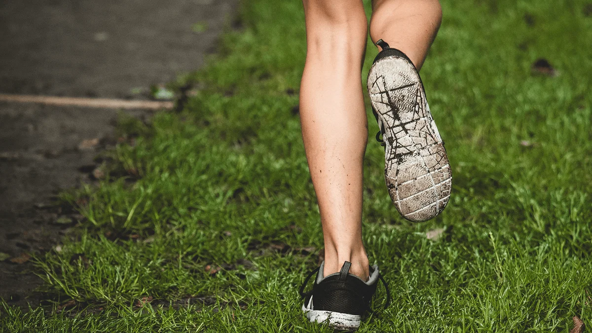 Corredor con zapatillas deportivas sucias trotando sobre el pasto verde