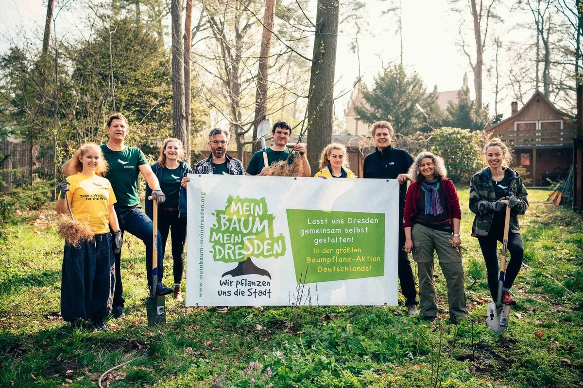 Group of ten people holding shovels and a banner promoting 